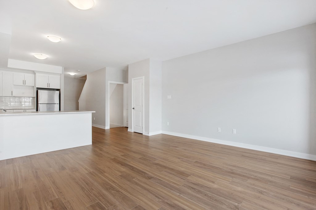 the living room and kitchen of an apartment with white walls and wood flooring
