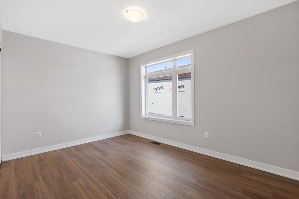 a bedroom with white walls and wood floors and a window