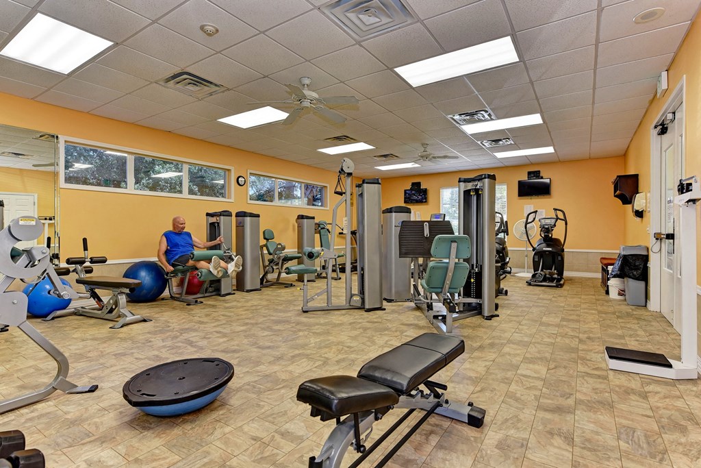 a gym with weights and cardio equipment and a man sitting on a chair