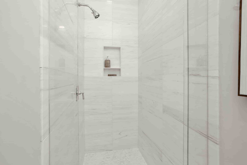 A white tiled shower with a shower head and a door.