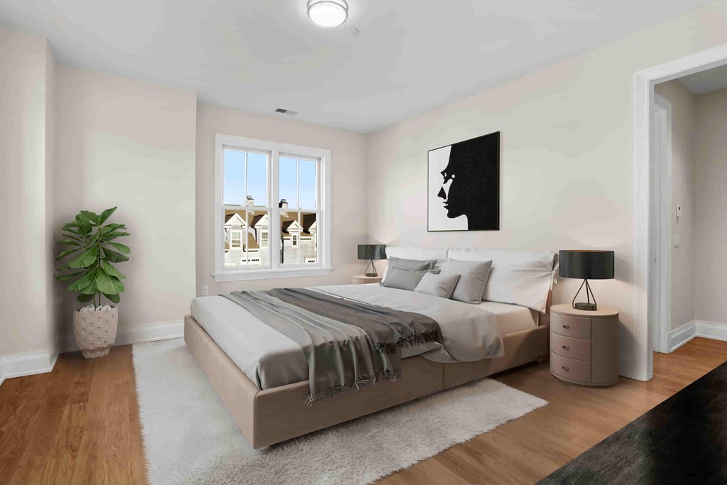 A bedroom with a large bed, a potted plant, and a window overlooking a residential area.