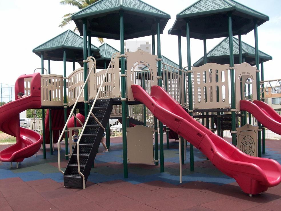 A playground with a red slide and a green roofed structure.