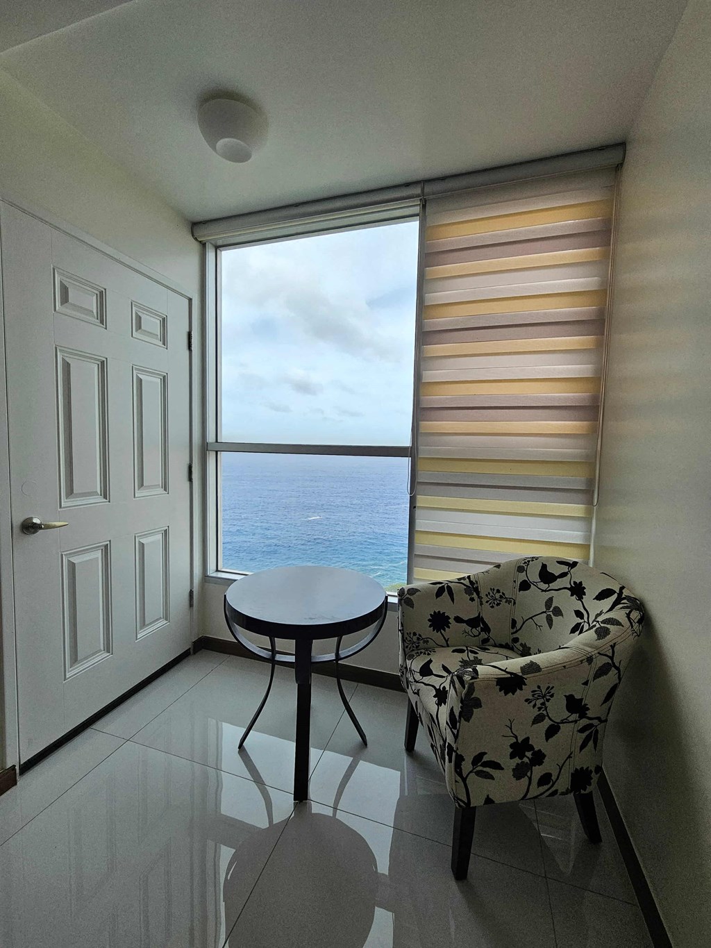 A room with a table and a chair facing a window with a view of the sea.