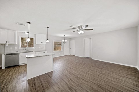 an empty living room with a kitchen and a ceiling fan