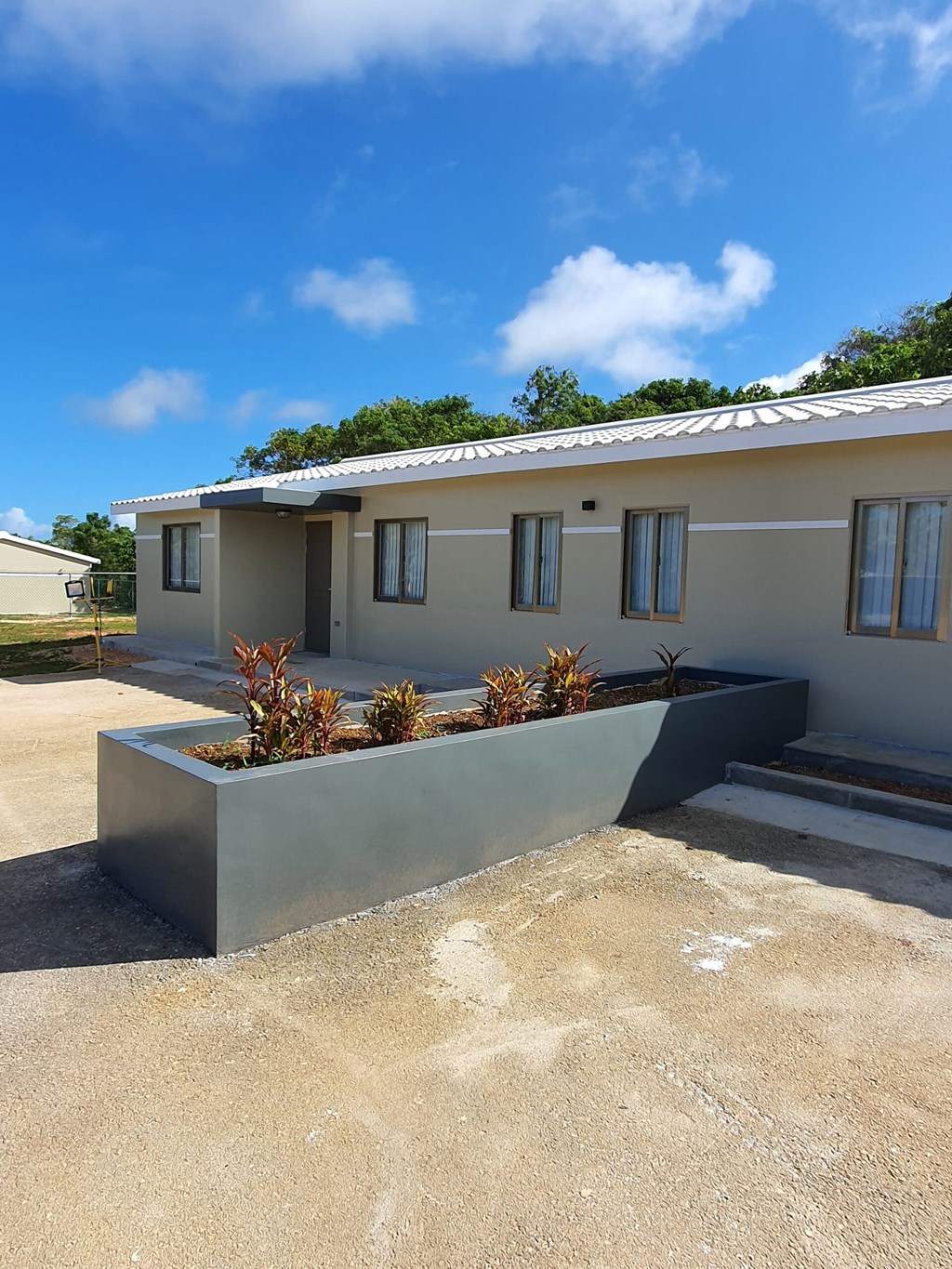 a white house with a concrete wall and plants in front of it