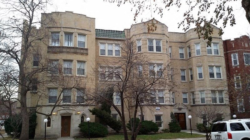 A large, beige building with a green roof and a white car parked in front.