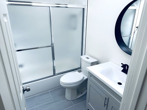 A white toilet is in a bathroom with a white sink and a round mirror.