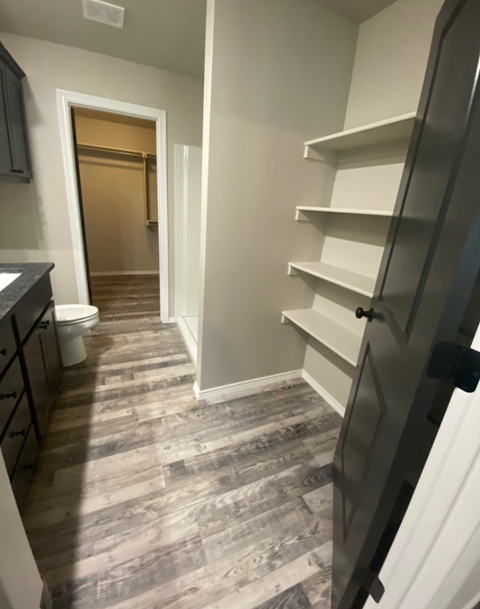 a walk in closet in a bathroom with a toilet and shelves