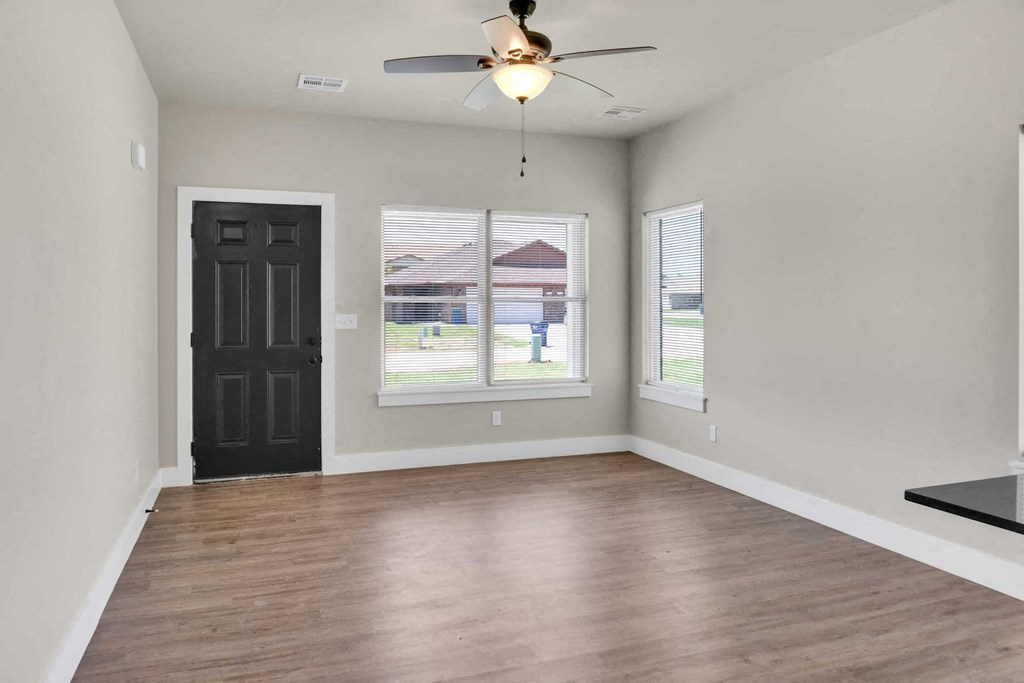 an empty living room with a ceiling fan and two windows