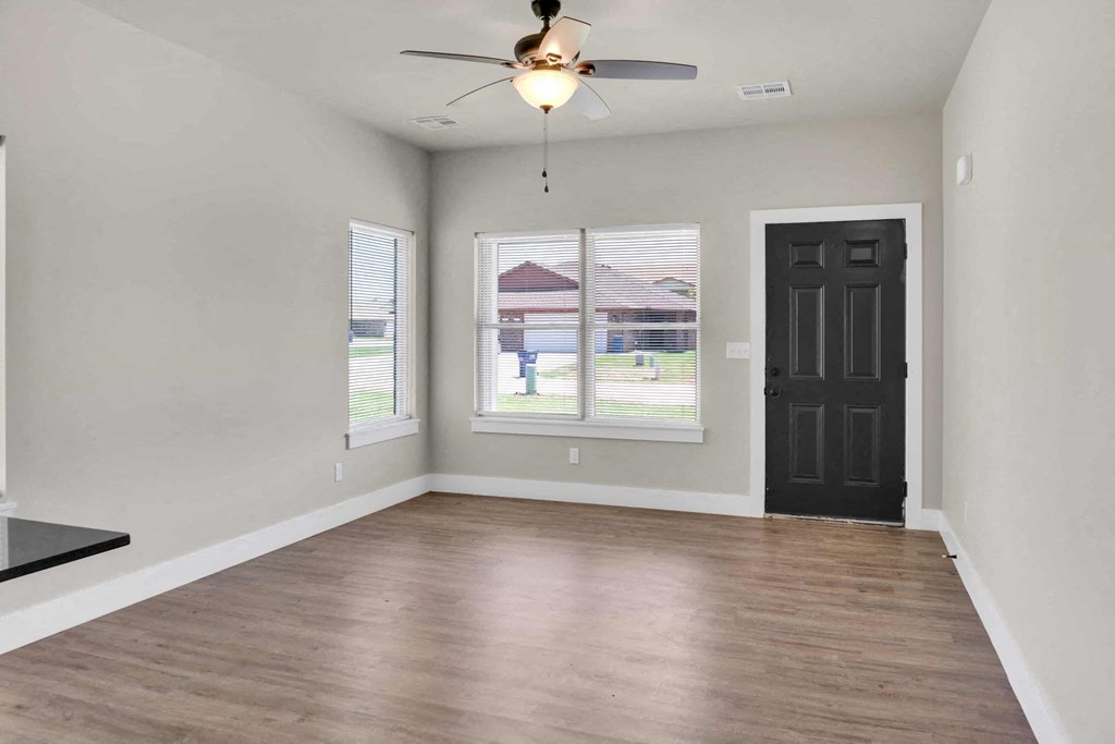an empty living room with a black door and a ceiling fan