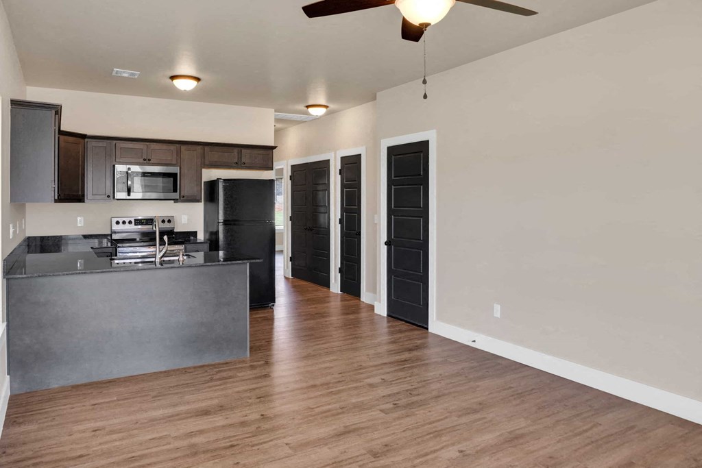 an empty living room with a kitchen and a ceiling fan