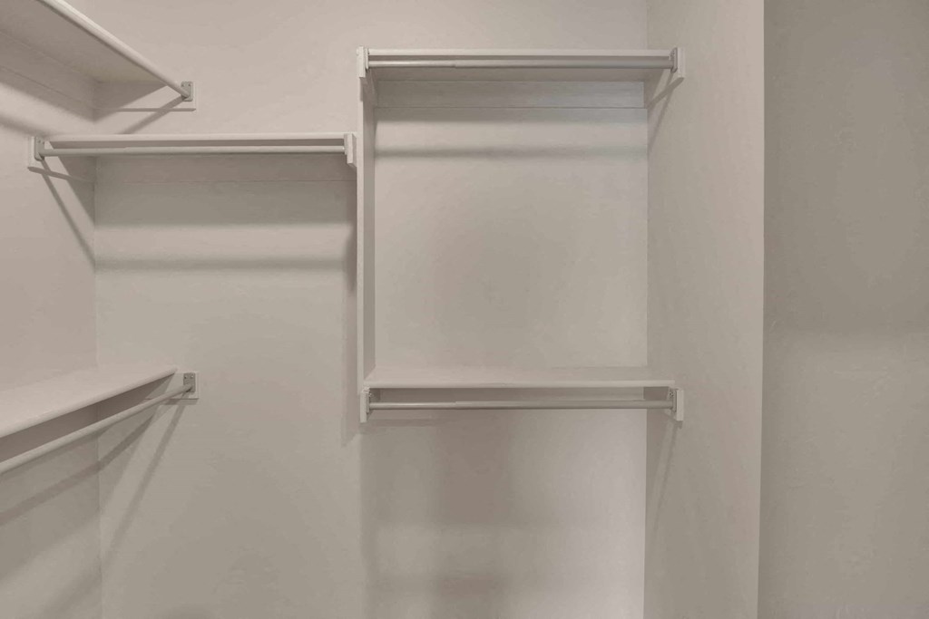 a walk in closet with white walls and shelves and a white closet door