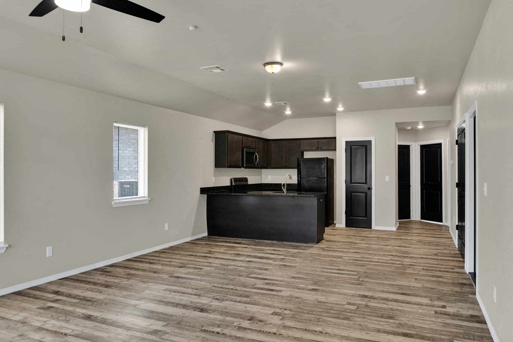 an empty living room with a kitchen and a ceiling fan