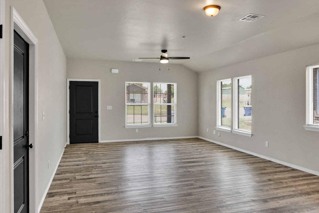 an empty living room with a black door and a ceiling fan