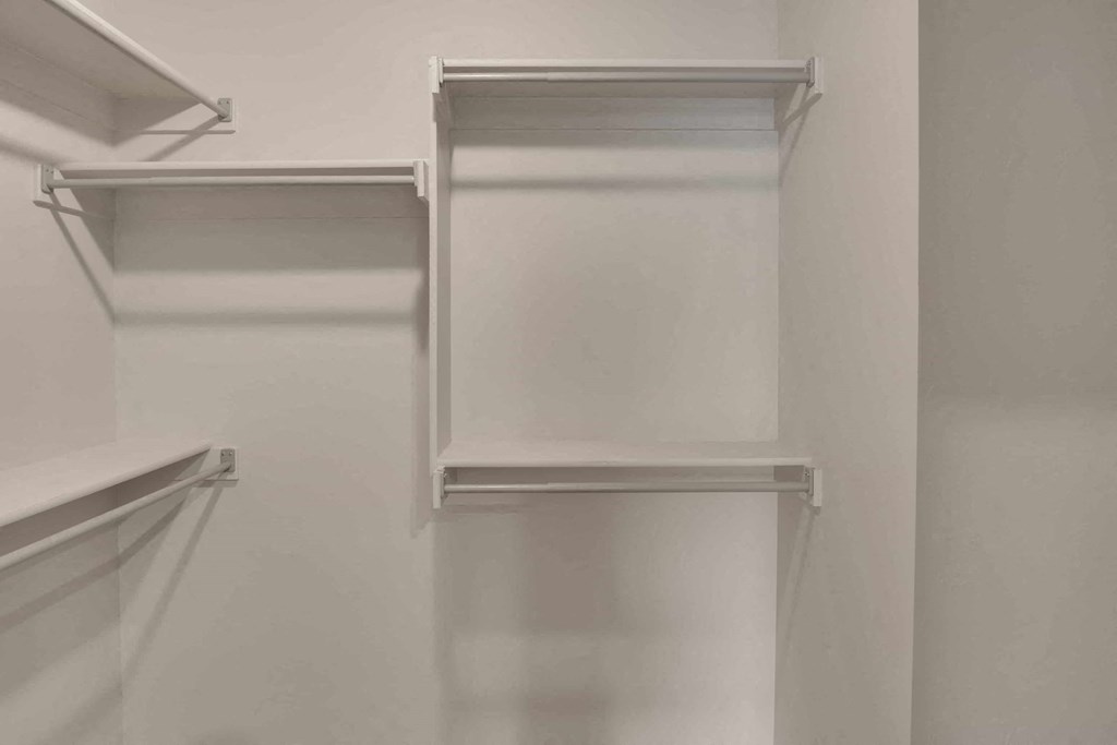 a walk in closet with white walls and shelves and a white closet door