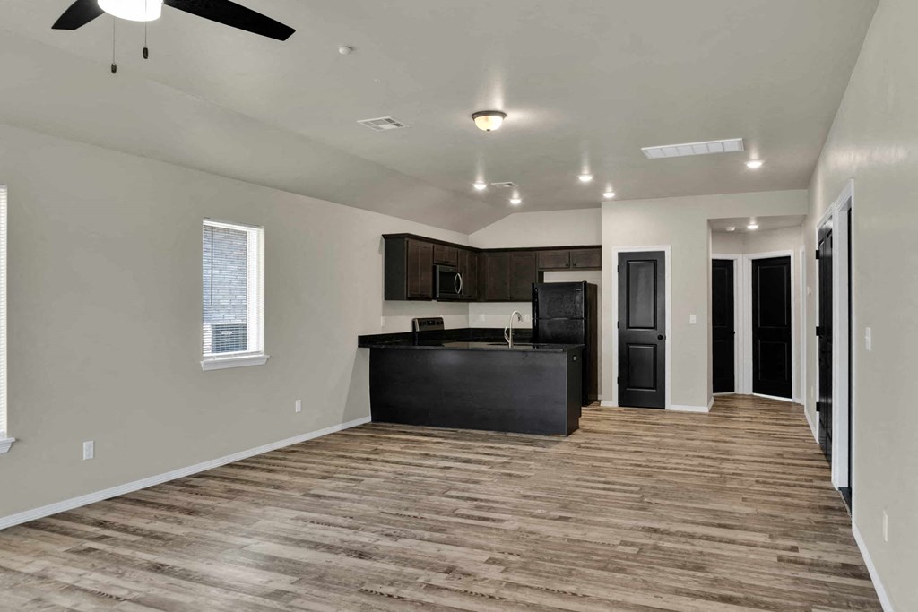 an empty living room with a kitchen and a ceiling fan