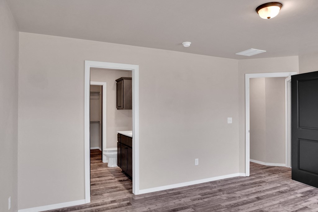 an empty living room with a hallway to a bathroom and a kitchen