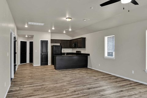 an empty living room with a kitchen and a ceiling fan