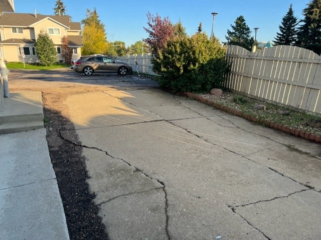 a crack in the sidewalk of a street with a fence