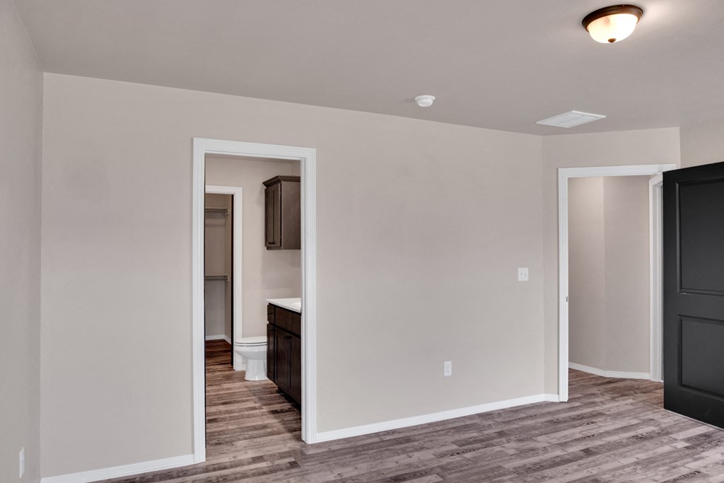 an empty living room with a hallway to a bathroom and a kitchen