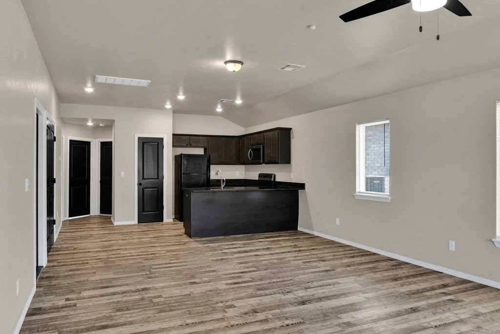 an empty living room with a kitchen and a ceiling fan