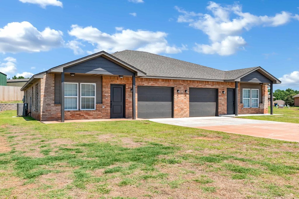 a brick house with two garage doors and a lawn
