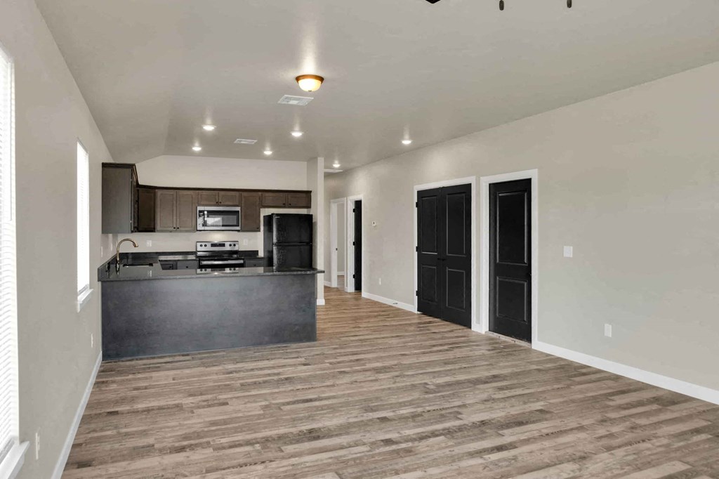 an empty living room with a kitchen with a counter top and a refrigerator