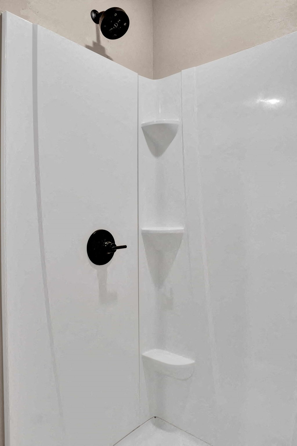 a shower with white walls and a black valve in it