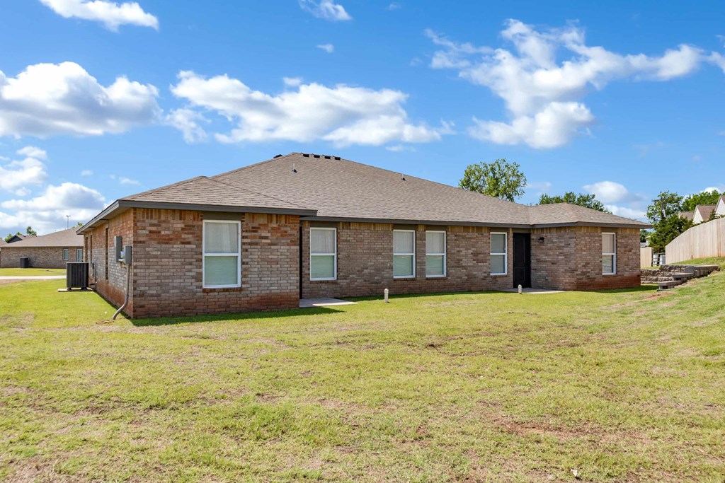 a brick house with a grassy yard and a cloudy sky