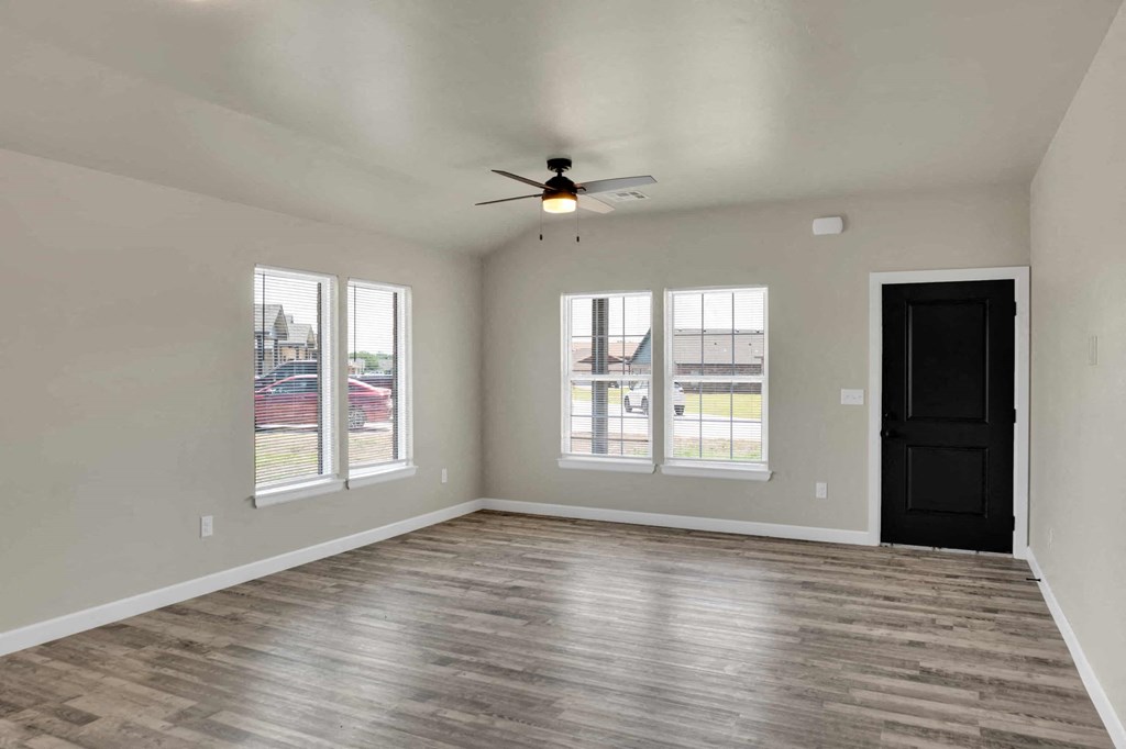 an empty living room with a ceiling fan and three windows