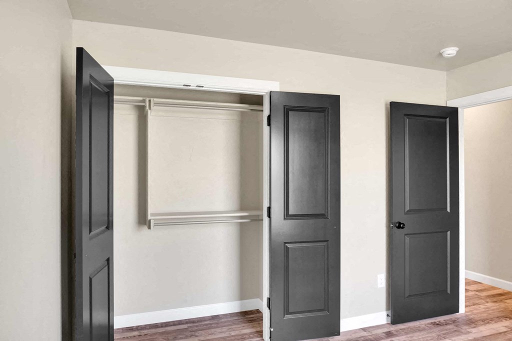 a closet with black doors and white walls and wood floors