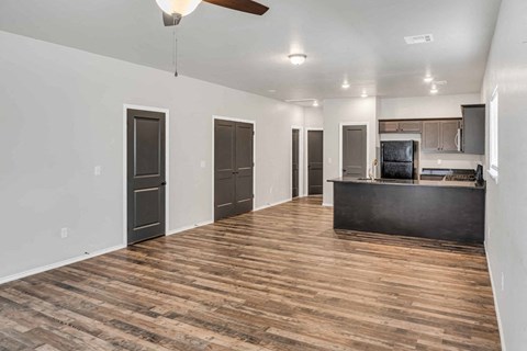 an empty living room with a kitchen and a ceiling fan
