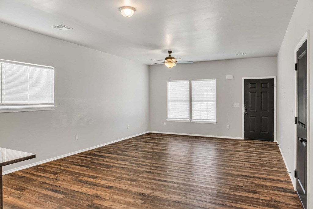 an empty living room with a black door and a ceiling fan
