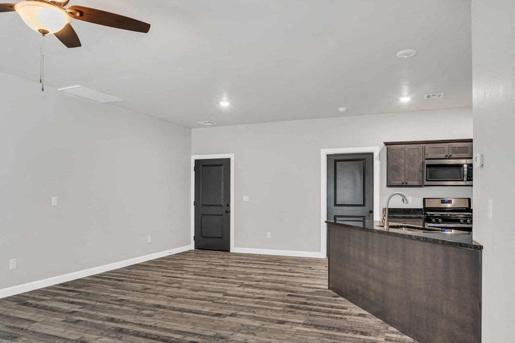 an empty living room with a kitchen and a ceiling fan