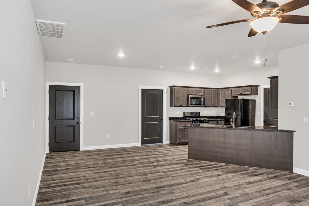 an empty living room with a kitchen and a ceiling fan
