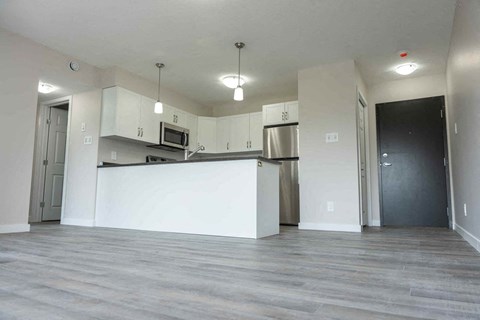 an empty living room and kitchen with white cabinets and a counter