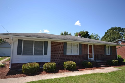 the front of a brick house with a porch and some bushes