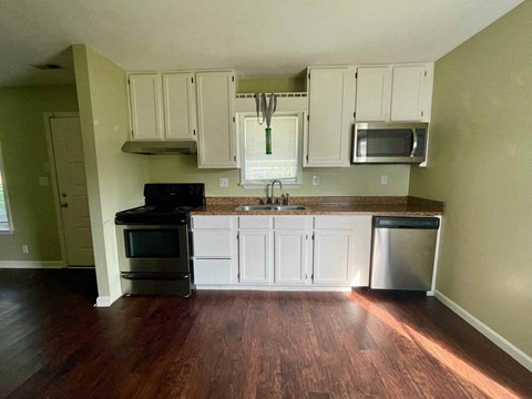 A kitchen with white cabinets and a wooden floor.
