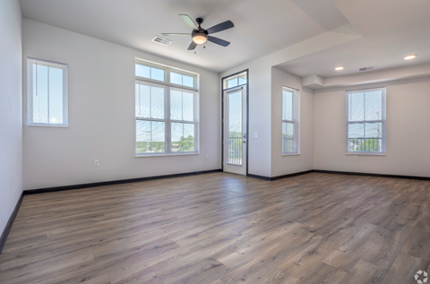 an empty living room with a ceiling fan and windows