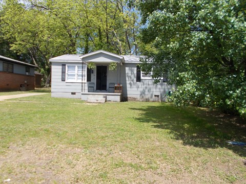 A small house with a porch is surrounded by trees and grass.