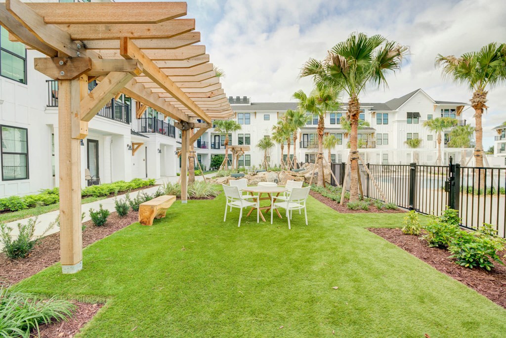 a backyard with a table and chairs under a wooden pergola