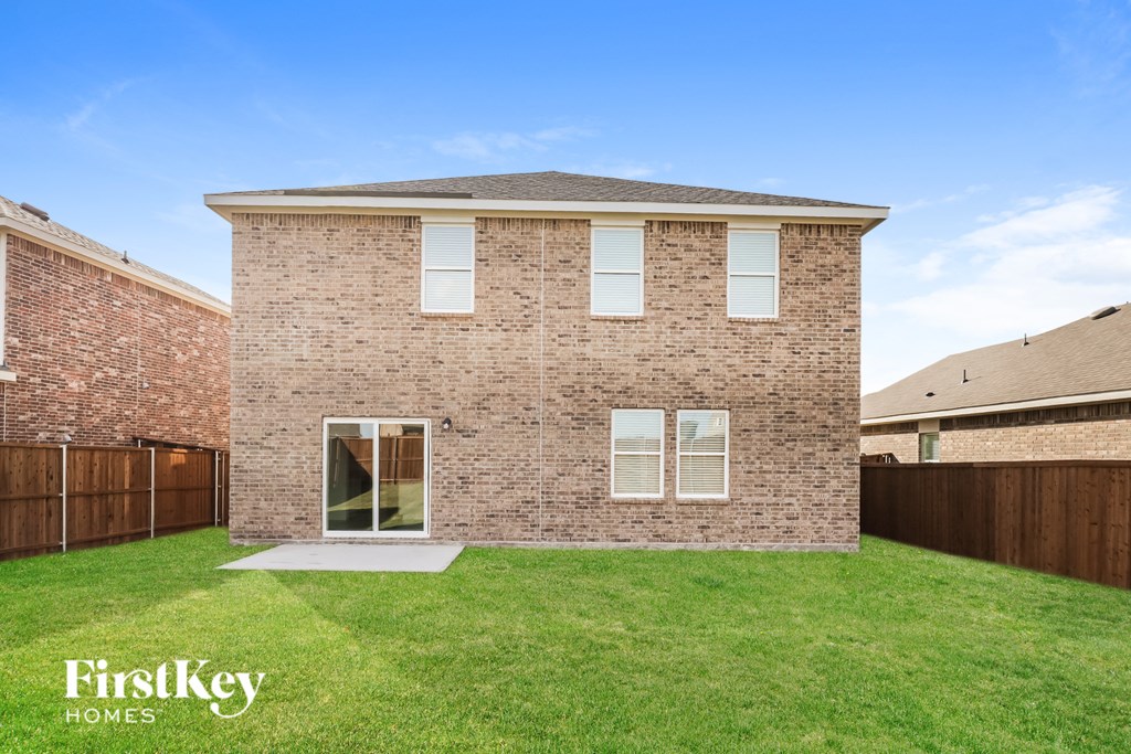 a small brick house with a grass yard and a wooden fence