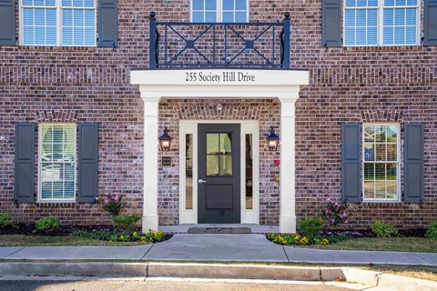 A brick building with a black door and windows with shutters.