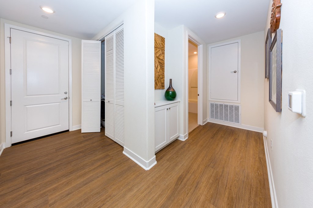 a living room with white walls and wooden floors and a hallway with white doors