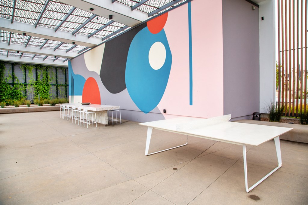 a room with white tables and benches in front of a wall with colorful paintings