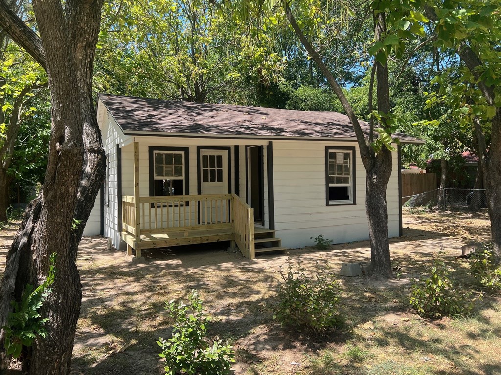 A small white house with a brown roof is surrounded by trees.
