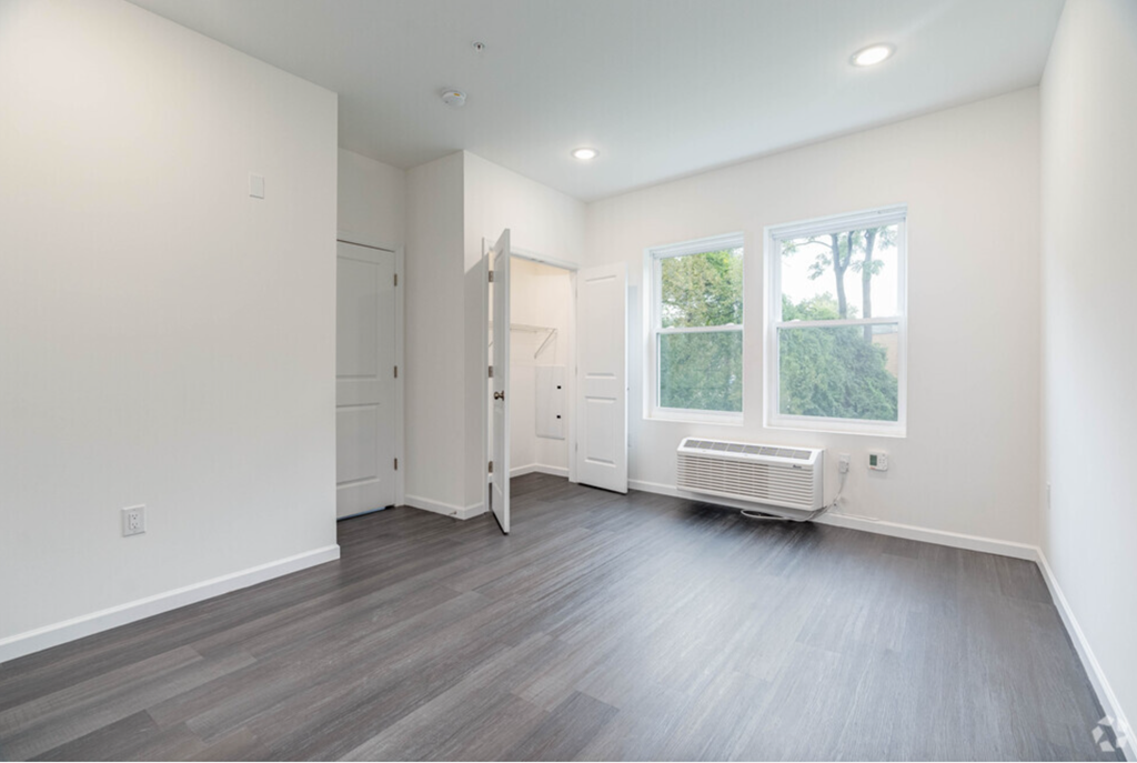 a living room with white walls and wood floors and a window