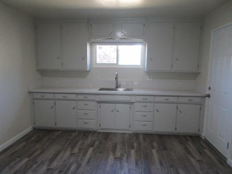 A kitchen with white cabinets and a wooden floor.
