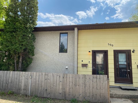 the front of a yellow house with a wooden fence