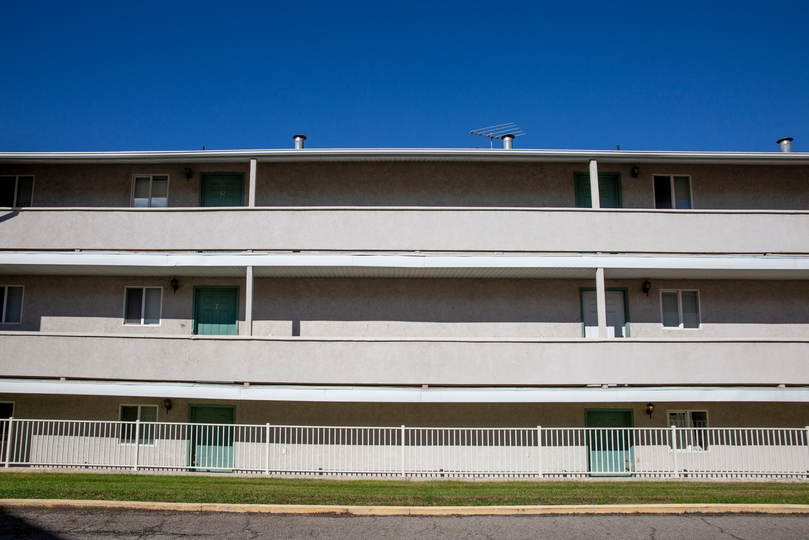 the side of a white building with green doors and a white fence